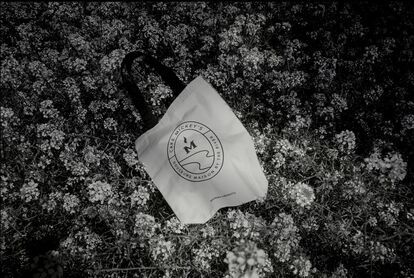 White tote bag with the Café Mickey's logo, placed on a bed of white flowers.