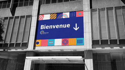 Large outdoor “Welcome” sign with downward arrow and “Together for Job Retention” logo, installed on the facade of a modern building, with colorful graphic banners featuring geometric designs.