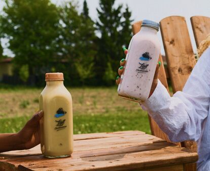 Photo of Lait Charbonneau milk bottles held outdoors on a wooden table, showcasing the product campaign created by Erod to highlight the brand’s artisanal quality and local authenticity.