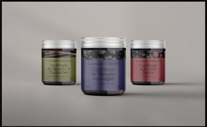 Trois pots en verre de confiture artisanale de La Maison du Bleuet alignés sur un fond gris. De gauche à droite : 