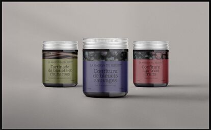 Three glass jars of artisanal jam from La Maison du Bleuet aligned on a gray background. From left to right: 