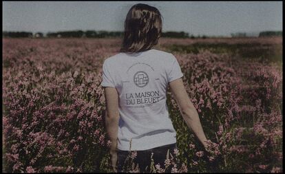 A person seen from the back, wearing a white t-shirt with the circular logo and the name 