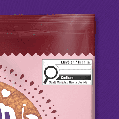 Close-up pink and red Mejicano packaging, Health Canada high in sodium label, black magnifying glass icon, bilingual text, textured purple background, serrated opening edge, partial view of food inside.